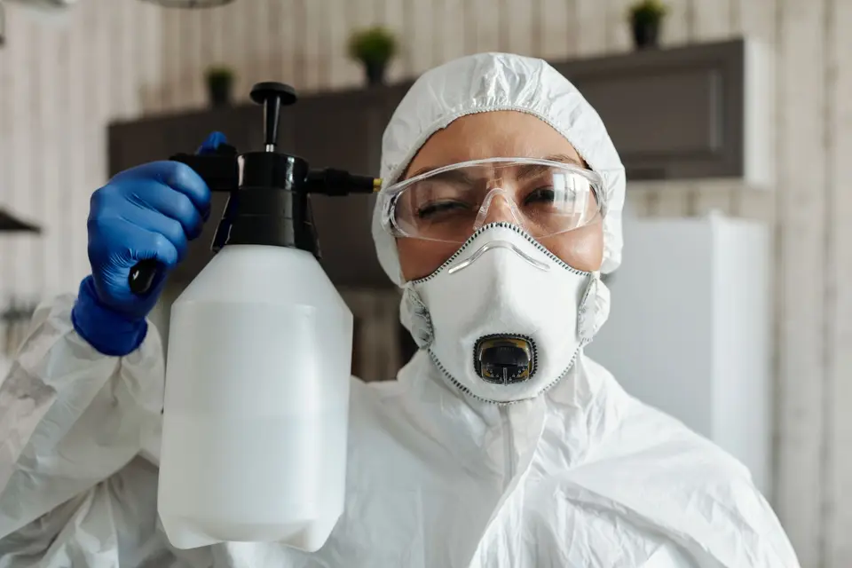 Intervenant en combinaison jetable, lunettes et masque, pulvérisateur à la main