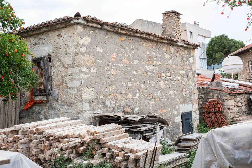 Matériaux de démolition entassés et bâchés au pied d'une maison en pierre